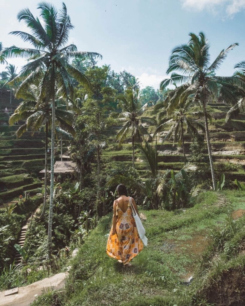 Danielle from the Wanderlover wearing a colorful orange dress while exploring Tegalalang rice paddies in Ubud Bali.
