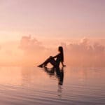 Silhouette reflection of a girl sitting at the edge of an infinity pool, surrounded by pink clouds