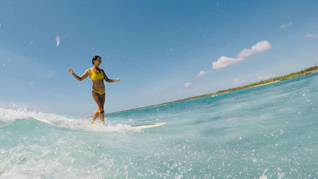 Girl on a surfboard cross stepping on a wave in clear blue waters.