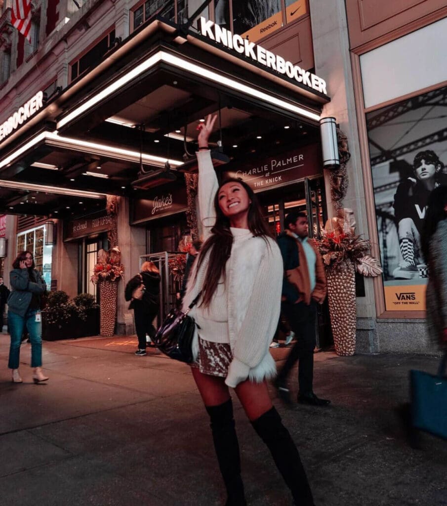 Girl smiling with hand up in the air in front of Knickerbocker Hotel