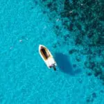 Drone shot of a boat in crystal clear blue waters in Comino Malta