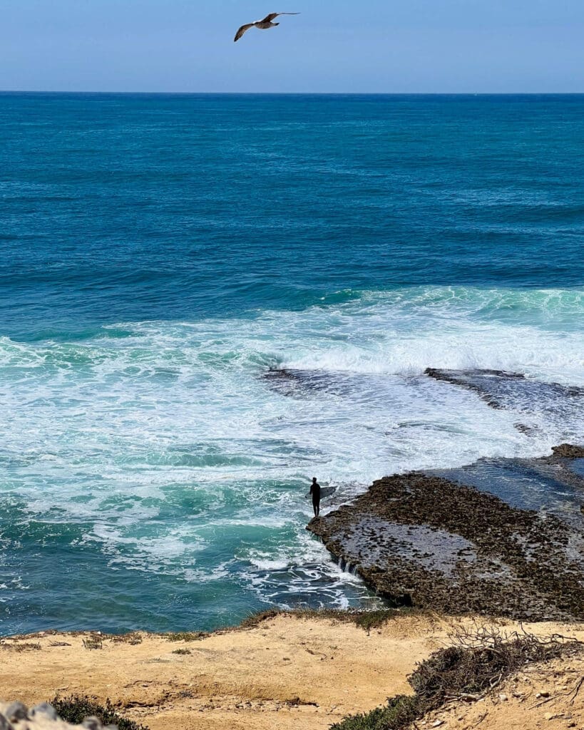 Man with surfboard standing on a rock about to go surf