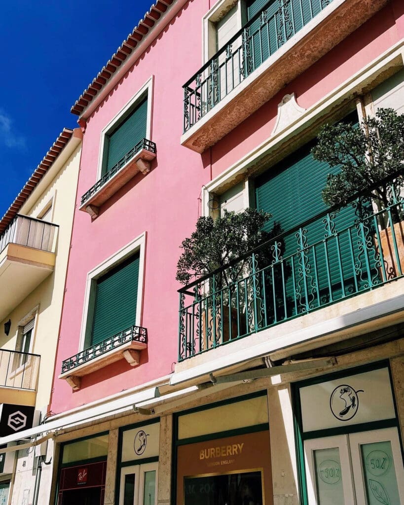 Pink building with a green door and floral balcony in Ericeira