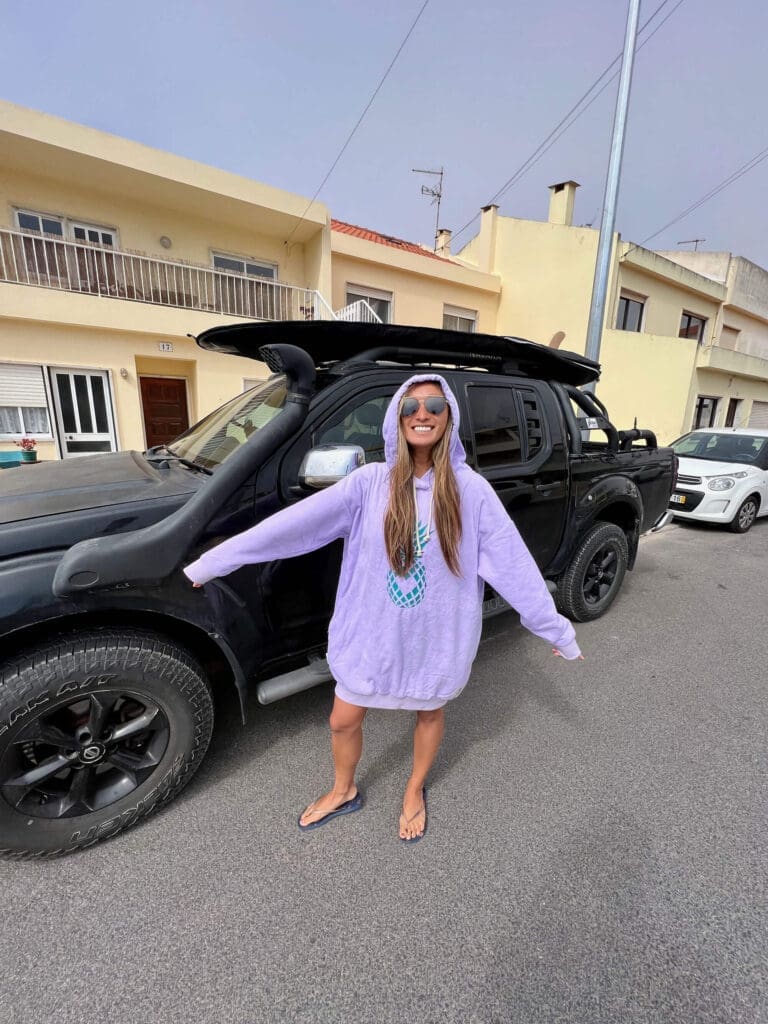 Girl in surf poncho in front of a truck with surfboard on top