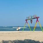 Surfer with surfboard walking on the beach with Chacahua swing in front