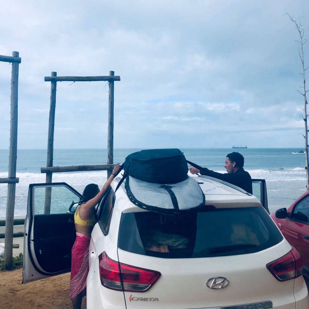 Two people strapping surfboards to roof of car