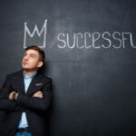 Man in front of blackboard with crown and word successful